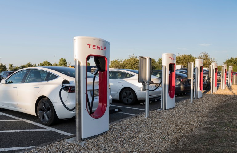 Grantham, Lincolnshire, England September 26, 2021: Line of Tesla electric car chargers with cars on charge at a motorway service area on a clear autumn evening in warm light from the setting sun.