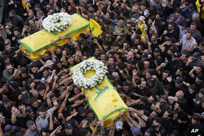 Hezbollah members carry the coffins of two of their comrades who were killed on Wednesday when a handheld device exploded,…