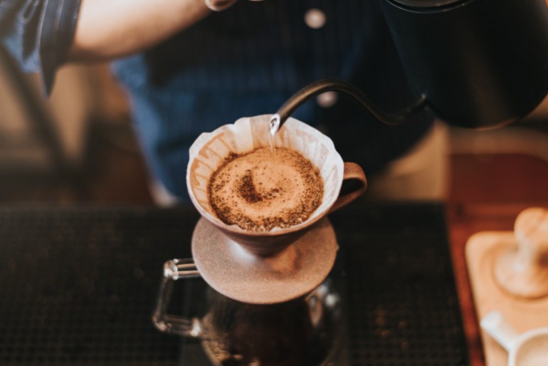 drip coffee, Barista making drip coffee by pouring spills hot water on coffee ground with prepare filter from copper pot to glass transparent chrome drip maker on wooden table in cafe shop