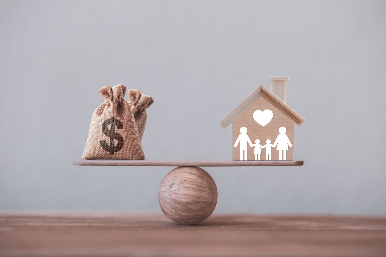 House mortgage and family financial management concept: Wooden home and heart, Family member, and US dollar hessian bags on a balance scale. Prepare expenses for the purchase of a residence. GettyImages-1254581657