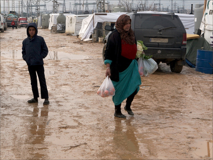 A Syrian refugee woman carries bags with supplies on a muddy road between makeshift shelters and tents in the informal Syrian refugee settlement Amriyeh in Saadnayel, Bekaa Valley, eastern Lebanon, which the European Union's ambassador to Lebanon Christina Lassen visited on 22 December 201