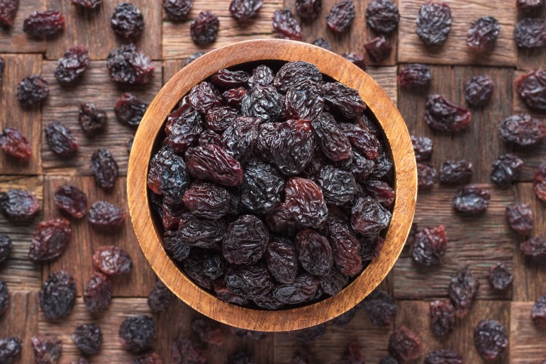 dried grapes, dark raisins in bowl on wooden table background. المصدر: أدوبي ستوك