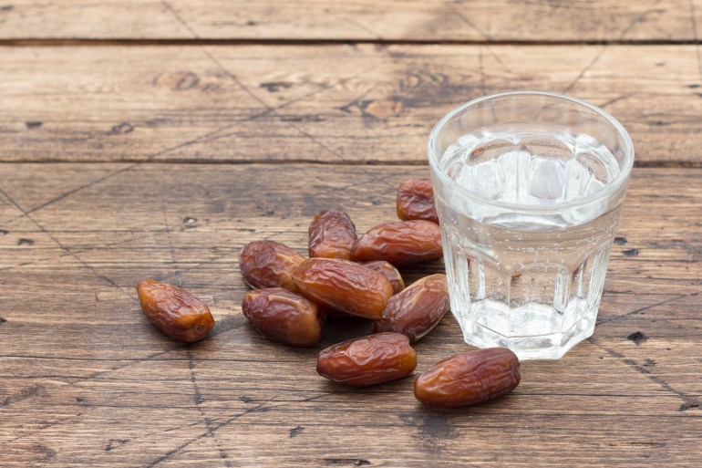 Dried dates fruits and a glass of water on a wooden table. Traditional fast breaking, Muslims evening meal during holy Ramadan