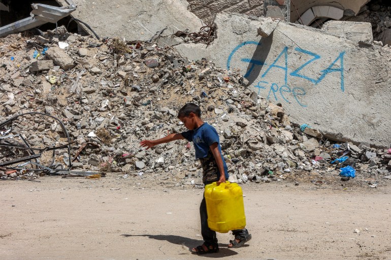 A boy walks carrying a jerrycan filled with water past the rubble of a destroyed building in Gaza City on April 21, 2025.