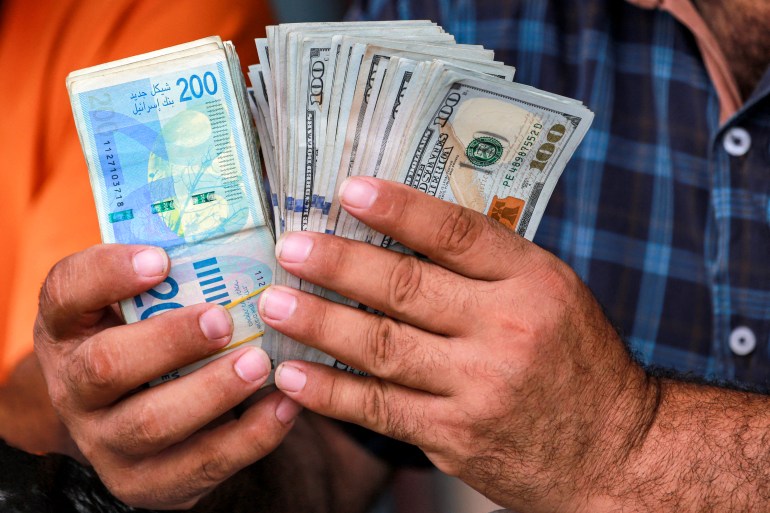 A man counts stacks of Israeli shekel and US dollar banknotes at an informal money exchange stall in Deir el-Balah in the central Gaza Strip on July 2, 2024 amid the ongoing conflict in the Palestinian territory between Israel and Hamas. (Photo by Bashar TALEB / AFP)