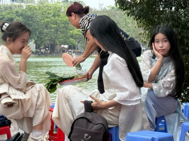 فتيات فتناميات خلال الايتعداد لجلسة بملابسهن التقليدية على ضفة بحيرة "هو هوان كيام" في قلب هانوي (الجزيرة)