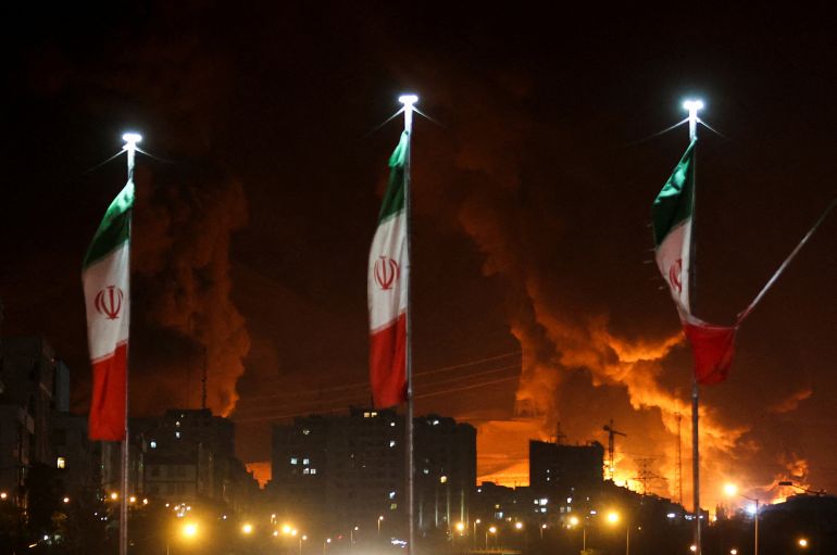 Iranian flags fly as fire and smoke from an Israeli attack on Sharan Oil depot rise, following Israeli strikes on Iran, in Tehran, Iran, June 15, 2025. Majid Asgaripour/WANA (West Asia News Agency) via REUTERS ATTENTION EDITORS - THIS PICTURE WAS PROVIDED BY A THIRD PARTY TPX IMAGES OF THE DAY