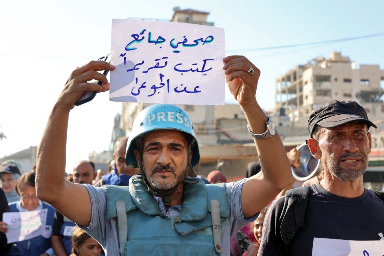 TOPSHOT - A demonstrator holds a sign reading in Arabic "a hungry journalist writes a report about the hungry" during a protest by journalists against hunger in the Rimal district of Gaza City on July 19, 2025.