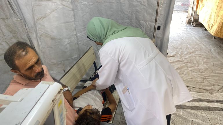 طبيبة تعاين طفلا مجوع يلقي برأسه على ساق والده المنهك من المجاعة-رائد موسى-دير البلح-الجزيرة نت