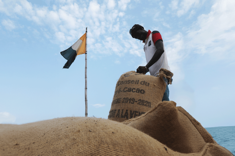 A worker sews up cocoa sacks next to an Ivory Coast flag in Soubre, Ivory Coast January 7, 2021. Picture taken January 7, 2021. REUTERS/Luc Gnago