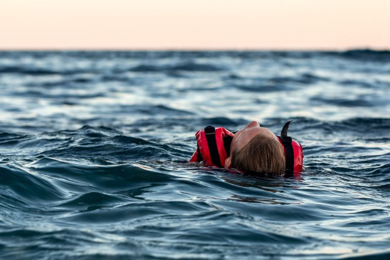 An unconscious drowning girl in a life jacket swims in a cold sea with waves at dusk. The danger of hypothermia. Rescue people on the waters. Man overboard on the high seas