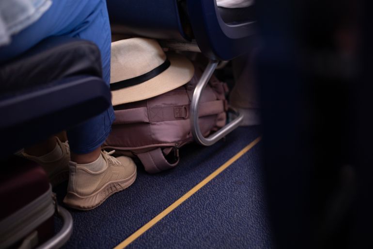 A person's legs and a suitcase are captured in the narrow space of an airplane aisle, emphasizing the cramped reality of air travel. Suitable for themes of travel, transportation, and the mundane aspects of journeys.