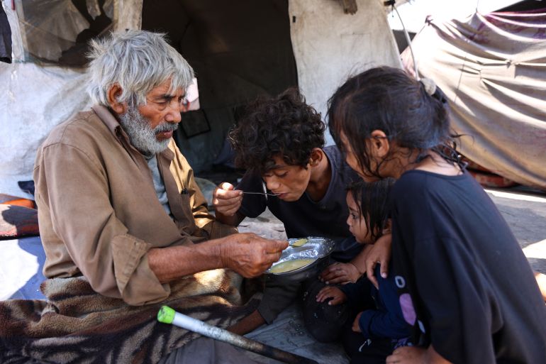 A Palestinian family share a bowl of lentil soup outside their tent in the Daraj neighbourhood in Gaza City on August 3, 2025.
