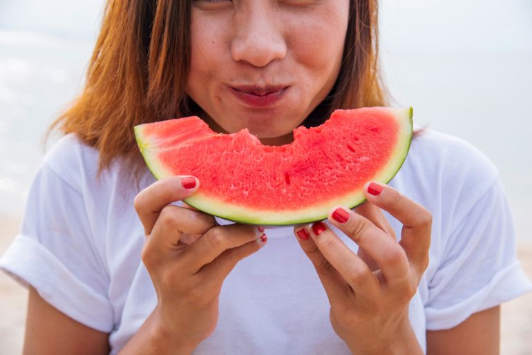 Women eat red watermelon organic hand holding red fruit high vitamins outdoor on tropical beach summertime. Young asian women smile enjoy eating tropical fruit happy time smile face. Female vegan; Shutterstock ID 2489188555; purchase_order: ajnet; job: ; client: ; other: