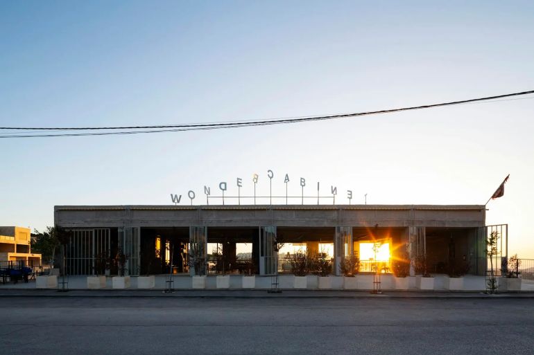 الواجهة الغربية عند شروق الشمس. تتميز بعناصر زخرفية بسيطة، تقتصر أساسًا على أحرف دوّارة مصنوعة من الفولاذ المقاوم للصدأ، موضوعة على السطح لتعمل كمؤشر للرياح (دوّارة رياح).