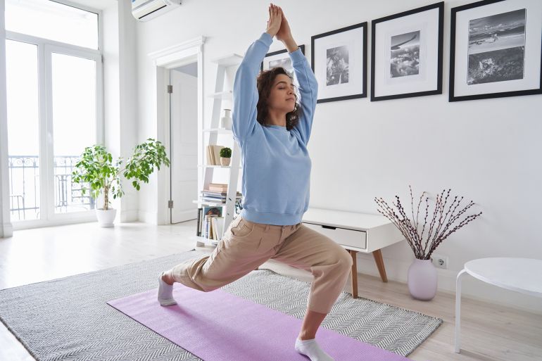 Fit healthy young woman doing pilates yoga exercise fitness training workout at home interior standing in warrior pose. Physical activity for body and mind relaxation, healthy lifestyle habits concept; Shutterstock ID 2013487703; purchase_order: aj; job: ; client: ; other: