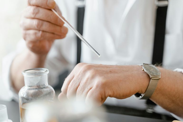 Close-up of a man using a dropper to apply fragrance on his wrist indoors
